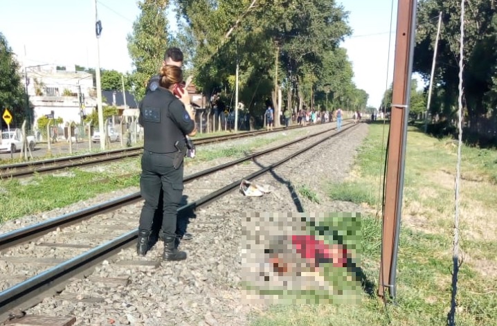 Los efectivos policiales observan al sospechoso del femicidio, que yace lesionado junto a las vías del tren.