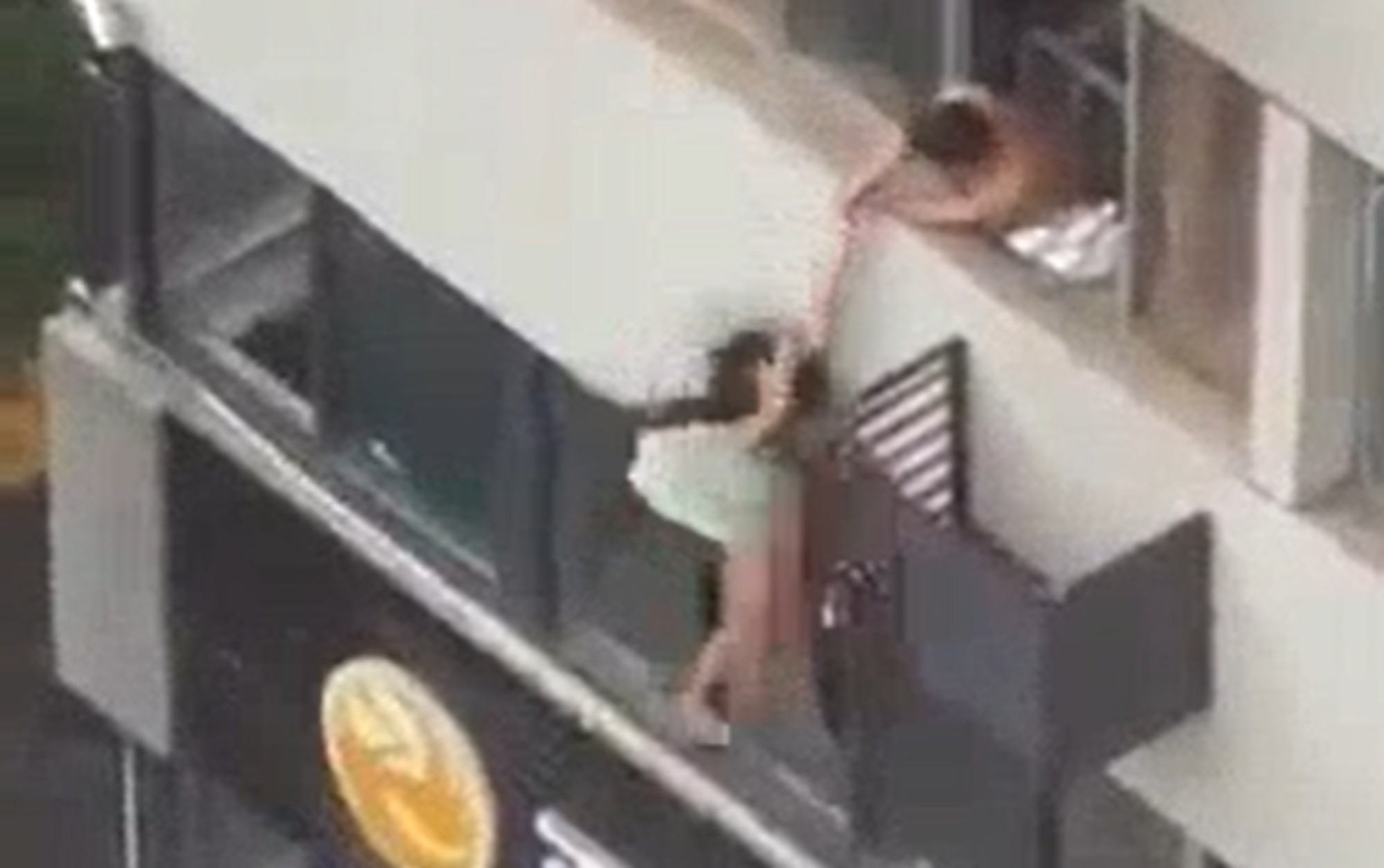 El video muestra la mujer balanceándose en el tercer piso del edificio, con un hombre intentando acercarla a la ventana.