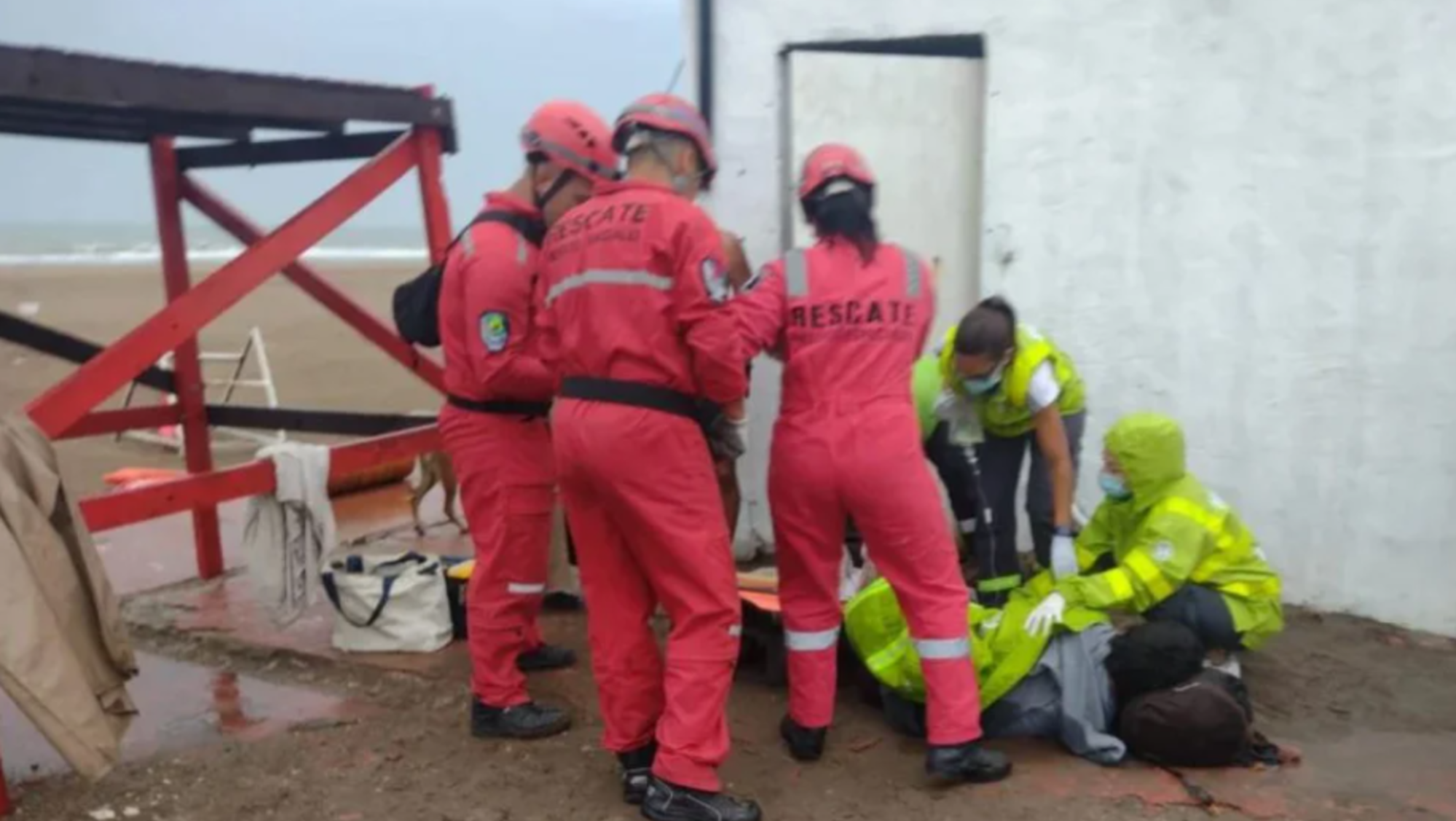 Personal de Bomberos del Puerto y Rescates Especiales de Mar del Plata atienden al hombre herido por una sombrilla clavada en su pierna.